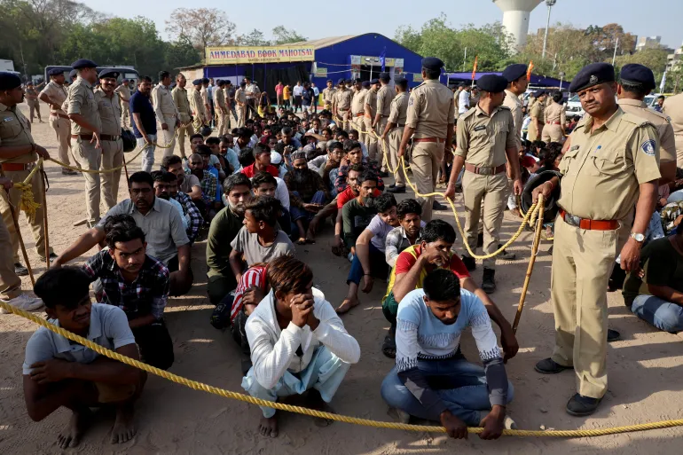 Police officers stand next to men they believe to be undocumented Bangladeshi nationals after they were detained during raids in Ahmedabad, India, on April 26, 2025