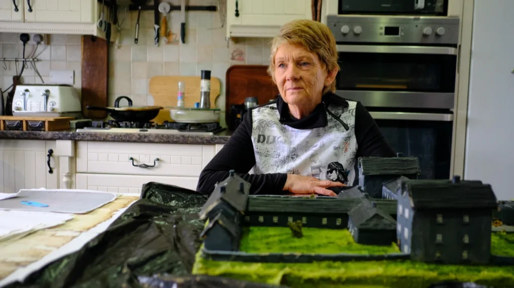 Local historian Catherine Corless sits with the clay model she made of the Tuam institution in her kitchen in rural County Galway. Corless said the start of the excavation has provided a sense of “relief.”