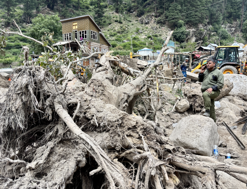 A man from the security forces speaking over phone beside the roots of a massive walnut tree that was swept into the village by the flash flood on August 14.
