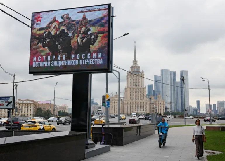 People walk near a banner in support of the Russian army in Moscow on August 11, 2025. The banner reads: ‘The history of Russia is the history of the defenders of the fatherland’