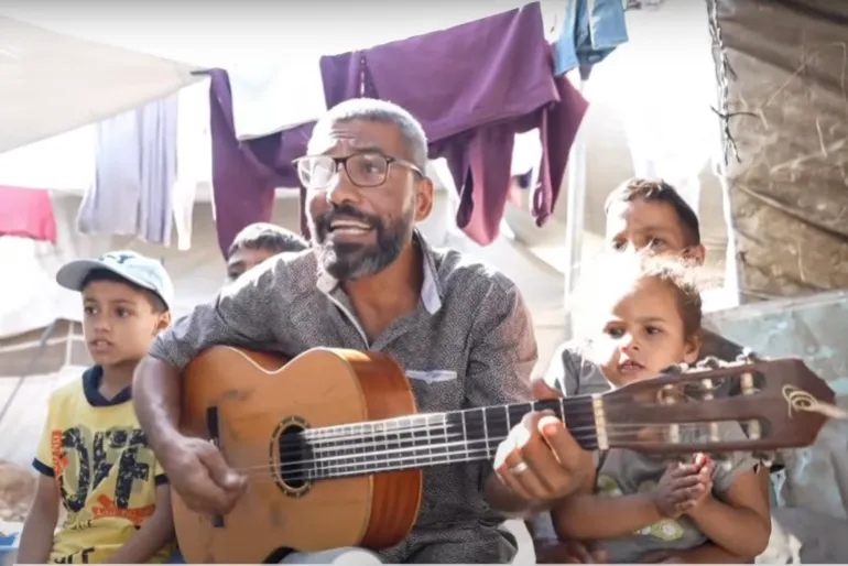 Musician Ahmed Abu Amsha sings with children in a makeshift camp in Gaza