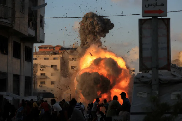 Palestinians react as smoke and flames rise while a residential building collapses after an Israeli air strike in Gaza City on September 7