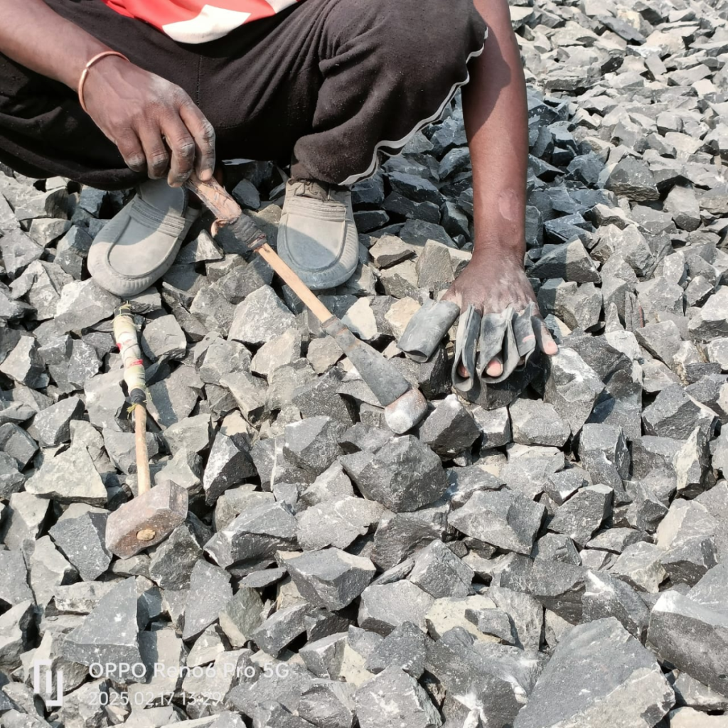 A worker crushing stones with bare hands protected by tyre made finger protectors.